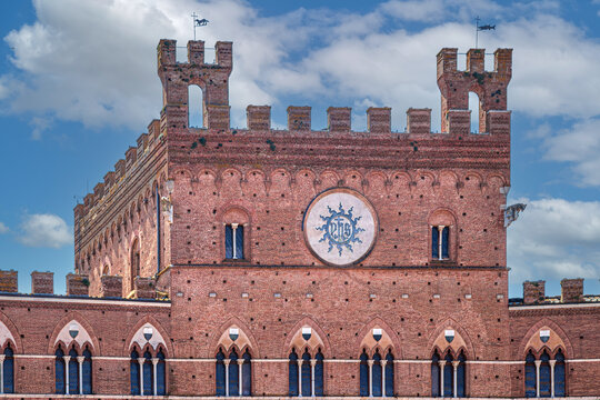 Detail of Palazzo Pubblico in Siena, Italy, featuring the IHS Christ monogram, red-brick Gothic fa&ccedil;ade, Guelph battlements, and medieval trifora windows in Piazza del Campo.