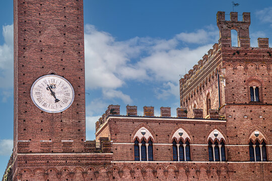 Palazzo Pubblico and Torre del Mangia in Siena, Tuscany, Italy, overlooking Piazza del Campo, showcasing Gothic architecture, red-brick facades, crenellations, and the iconic clock tower.