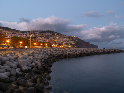 Rocky breakwater and hillside city lights at dusk in Funchal, Madeira, Portugal