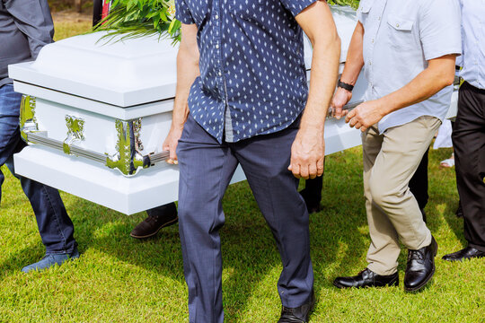 Family friends carry coffin during burial ceremony in green outdoor setting