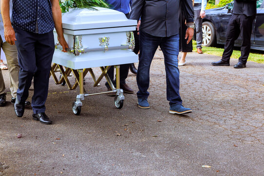 Group carries casket on wheeled stretcher in cemetery during burial ceremony