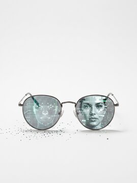 Round metal eyeglasses reflecting wireframe face scan and pixelated human portrait on lenses, AI facial recognition concept