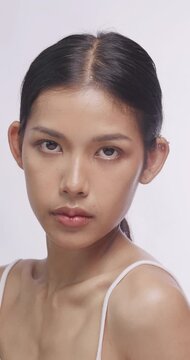 Young Asian woman touching her neck and shoulder gently. She poses gracefully in studio light.