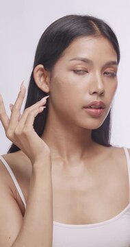 Asian model applying facial cream on her cheek. She gentley massages her smooth skin in studio.