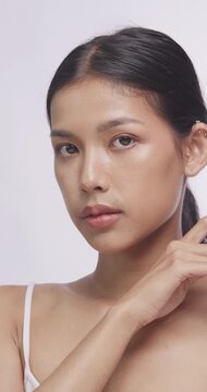 Asian model gently touching her face with both hands. She looks closely at camera with flawless skin.