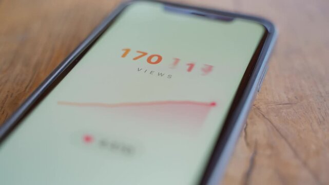 Analytics app on smartphone showing rising view counter and growth chart on a wooden table