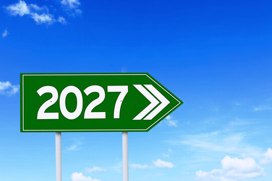 Green Road Sign Pointing to 2027 Year Against Clear Blue Sky