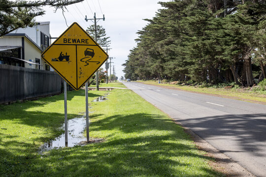 Warning sign reading&nbsp;"BEWARE" with symbols for agricultural machinery and slippery road conditions, standing on side of a country road in Werribee South, Melbourne, Victoria, Australia