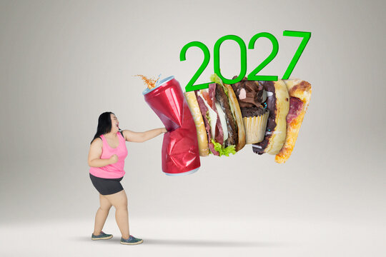 Overweight Woman Punching Fast Food and Soda Can with 2027 Text for Healthy New Year Resolution