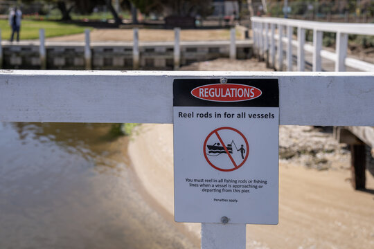 A regulation sign reads &ldquo;Reel rods in for all vessels&rdquo; on pier railing at Werribee South Beach, Melbourne, Australia. Shared use of waterways by boats and anglers, boating safety and fishing etiquette