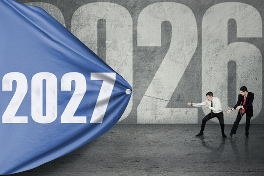 Businessmen Pulling Blue Banner with 2027 to Cover 2026 on Concrete Wall