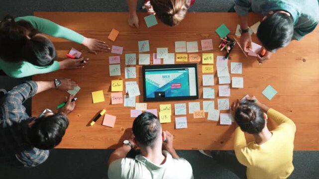 Top down view of programmer brainstorming and planning about web design while looking at tablet wireframe prototype. Aerial view of skilled developer team talking about digital application. Symposium.