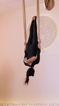 Vertical video. Body balance. Hammock yoga. Woman hanging upside down doing synchronous fitness session in studio rotating with equipment support.