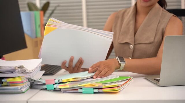 Organized Chaos: A dedicated professional meticulously sorts through a large stack of documents and files at her desk.