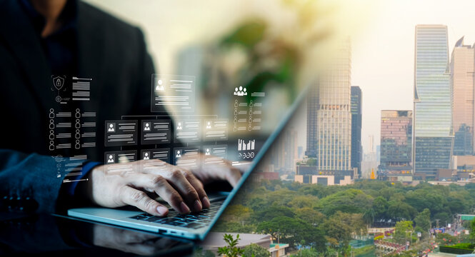 Business person typing on a laptop with virtual organizational chart and employee profile icons against a city background. Concept of human resources management, corporate hierarchy, and recruitment.
