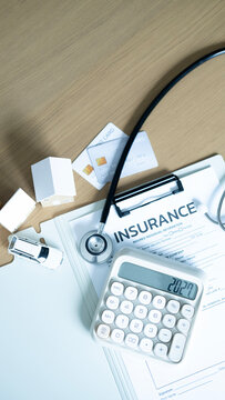 Top view of insurance document, calculator, stethoscope, credit cards, miniature houses and toy car on wooden table. Medical expenses, property protection and insurance financial planning concept.