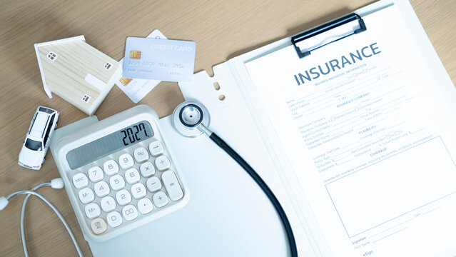 Insurance application form with calculator, stethoscope, credit cards, miniature house and toy car on wooden table. Healthcare coverage, property insurance, financial plan and risk protection concept.