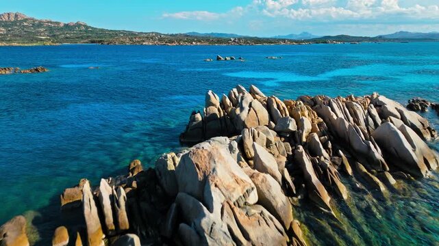 Drone view of Spiaggia Testa del Polpo coastline in Sardinia. Granite rock formations, deep blue sea and distant islands create a dramatic La Maddalena seascape.