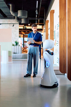 Man using a digital tablet while interacting with an advanced service robot in a contemporary office or retail space