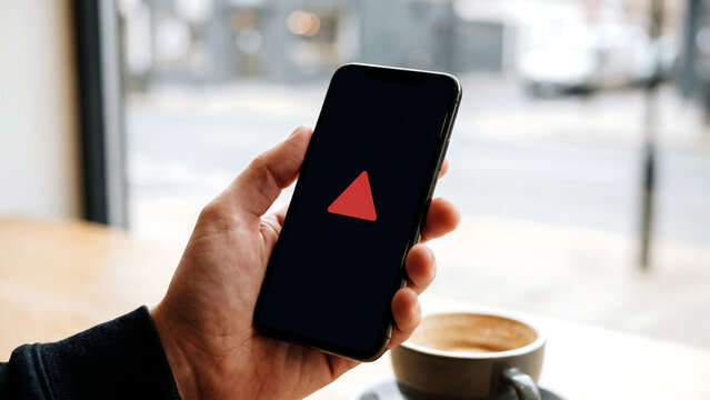 カフェの窓辺で赤い三角マークが表示されたスマートフォンを持つ手