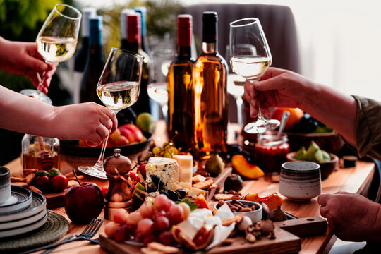 White wine glass holding during lunch with friends at dinner table. Food pairing with gourmet cheese appetizer board. Celebration and hospitality lifestyle at home party event.