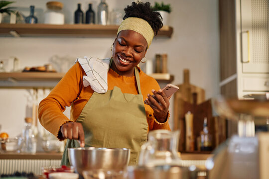 Black woman cooking recipe at home using smartphone