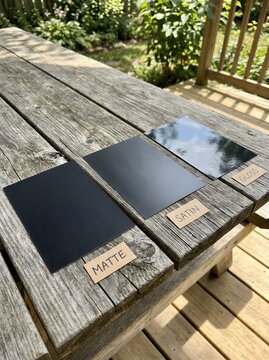 Three different finishes of metal sheets on a rustic wooden table outdoors.