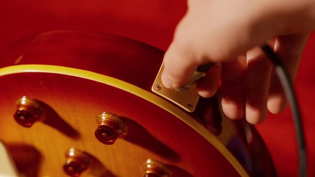 Slow motion shows a hand unplugging an audio cable from an electric guitar.