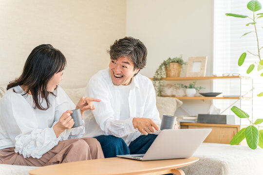 Couple Sitting on a Sofa at Home, Drinking Coffee and Looking Surprised at a Computer