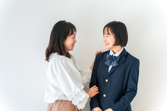 制服姿の高校生の娘に笑顔で寄り添う母親。入学や進学を迎える中学生。