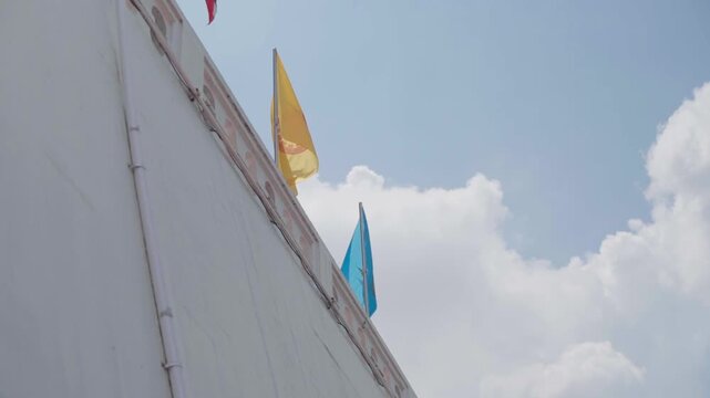 Slow motion yellow and blue flags waving on white temple wall against clouds