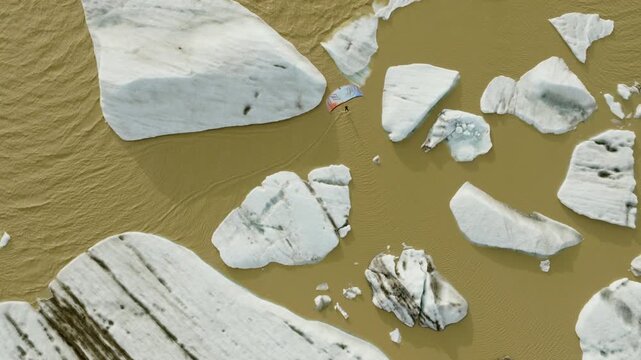 Kitesurfer crosses Fjallsarlon Glacier Lagoon, Oraefi, Hornafjordur, South Iceland, Iceland, between large floating ice formations below Fjallsjokull, drone top down tracking