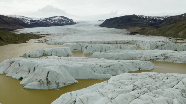 Fjallsarlon Glacier Lagoon, Oraefi, Hornafjordur, South Iceland, Iceland, shows Fjallsjokull ice front, floating ice, moraine and meltwater, drone forward flyover