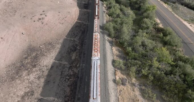 Train travels across arid land, passing by road and vegetation
