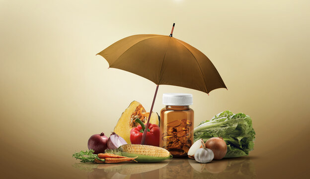 Amber supplement bottle protected by an umbrella surrounded by fresh vegetables on a warm beige background, representing health protection, nutrition, wellness, and preventive healthcare.