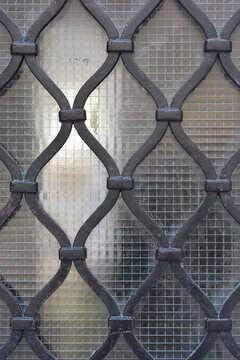 A close up shot of a classic dark metal security grille with a wavy pattern installed over textured safety wired glass.