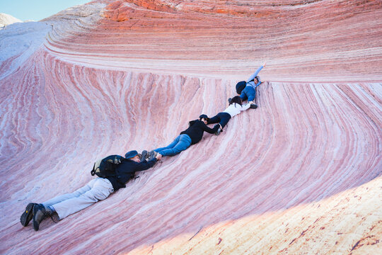 A group of hikers posting for fun photos of climbing along the striated sandstone formation. White Pocket. Vermilion Cliffs National Monument. Arizona. USA.
