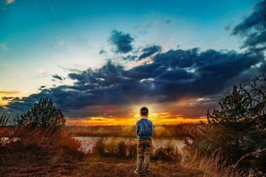 Young boy stands on a hill watching the sunset