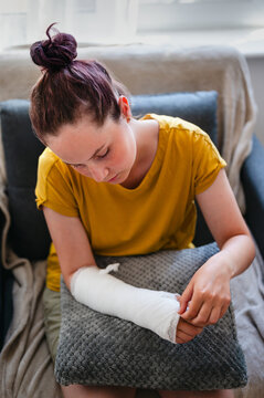 Teenage girl with injured arm in cast resting at home in an armchair