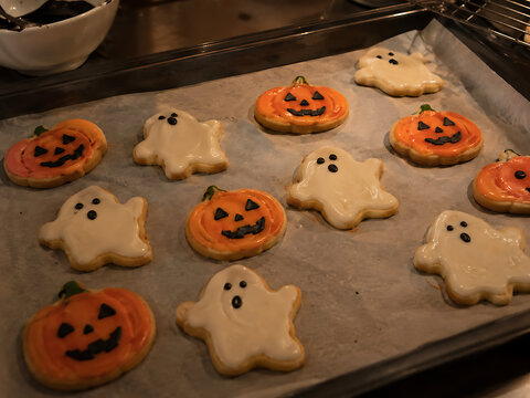 Decorated Halloween cookies in pumpkin and ghost shapes on a baking sheet