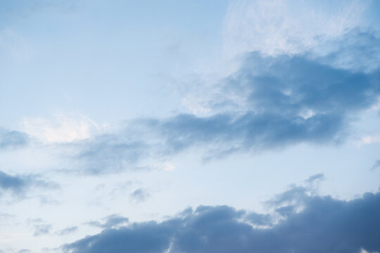 Stratocumulus clouds drift across a pale blue sky