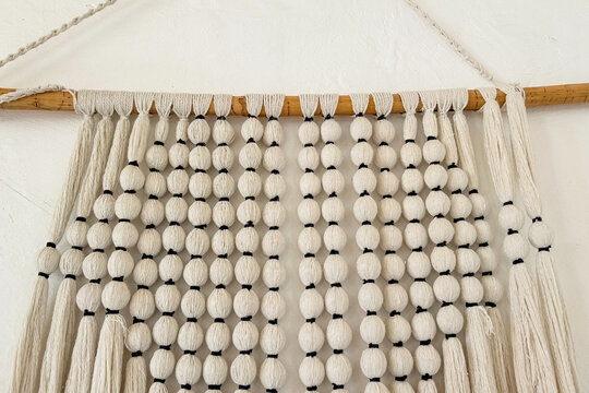 Macrame wall hanging with cotton rope spheres and wooden rod against a plain white wall background