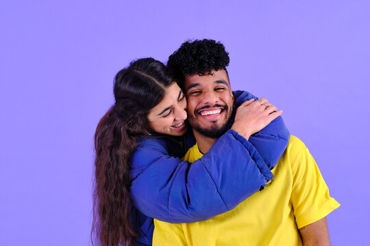 Young diverse couple embracing and smiling on purple background