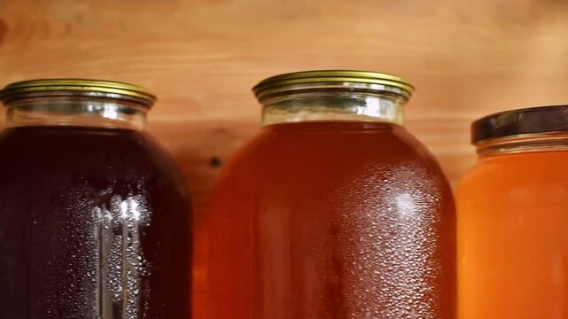 The camera gently pans along colorful jars of homemade fruit juice and compote on a wooden shelf.