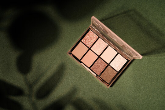 Eye shadow palette with neutral shades on a textured green background with leaf shadows