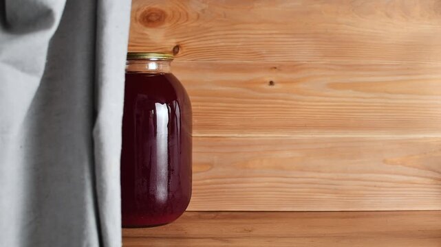 A person places jars of homemade fruit juice and compote one by one onto a wooden pantry shelf.