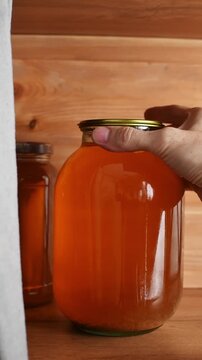 A hand grasps and turns a large jar of homemade fruit compote on a shelf to inspect its contents.