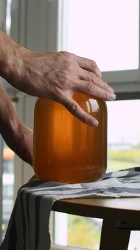 A person sets a jar of homemade fruit compote on a towel and gently wipes the glass and lid clean.