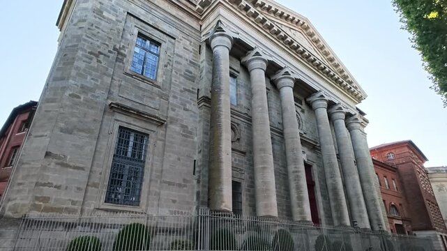Low-angle walking shot toward Notre-Dame de la Daurade or Basilique Notre-Dame de la Daurade neoclassical stone facade with six tall columns and a triangular pediment, Toulouse, France