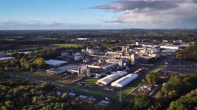 Aerial footage of large industrial complex, chemical production plant, and manufacturing factory facilities surrounded by green fields and rural landscape in Hamm Uentrop, Germany.